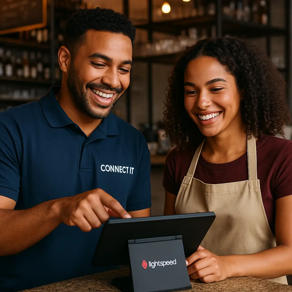 Technicien antillais CONNECT IT en polo bleu expliquant avec le sourire à une serveuse métissée comment utiliser la tablette Lightspeed POS sur un comptoir de restaurant tropical.